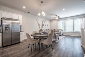 Een moderne keuken met een geïntegreerde koelkast, een eethoek met een ronde tafel en stoelen, en een zithoek met een bank en een plafondventilator.
