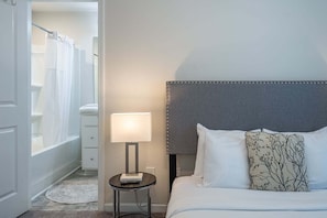 Een hotelkamer met een bed, een nachtkastje met een lamp, een nachtkastje en uitzicht op de badkamer.