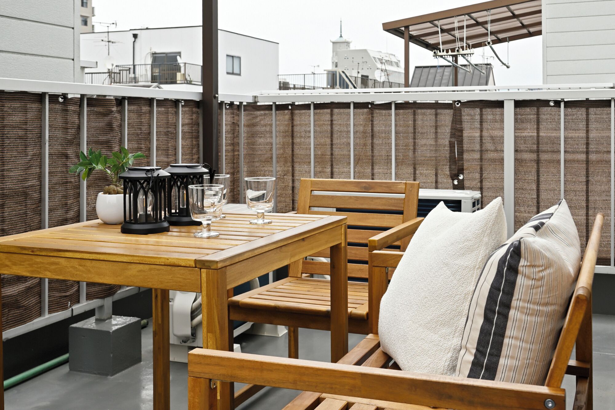 A wooden table with chairs and a small potted plant on a balcony with a view of buildings.