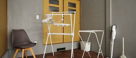 A room with a wooden door, a white drying rack, a small table, a chair, and a vacuum cleaner.