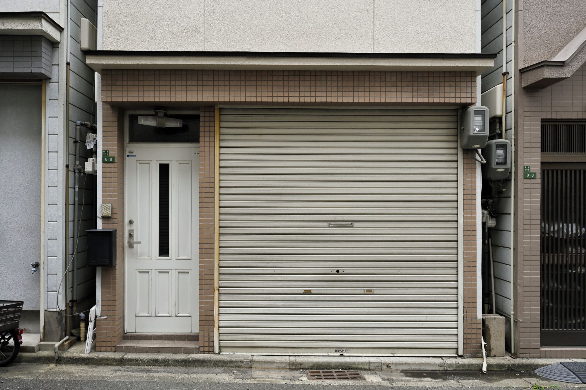 A closed metal roller door with a white door to the left, a small window above the door, and a utility box on the right.