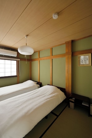 Ein Zimmer mit zwei Betten, einem Deckenventilator, einem Fenster mit Jalousien und einem gerahmten Bild an der Wand.
