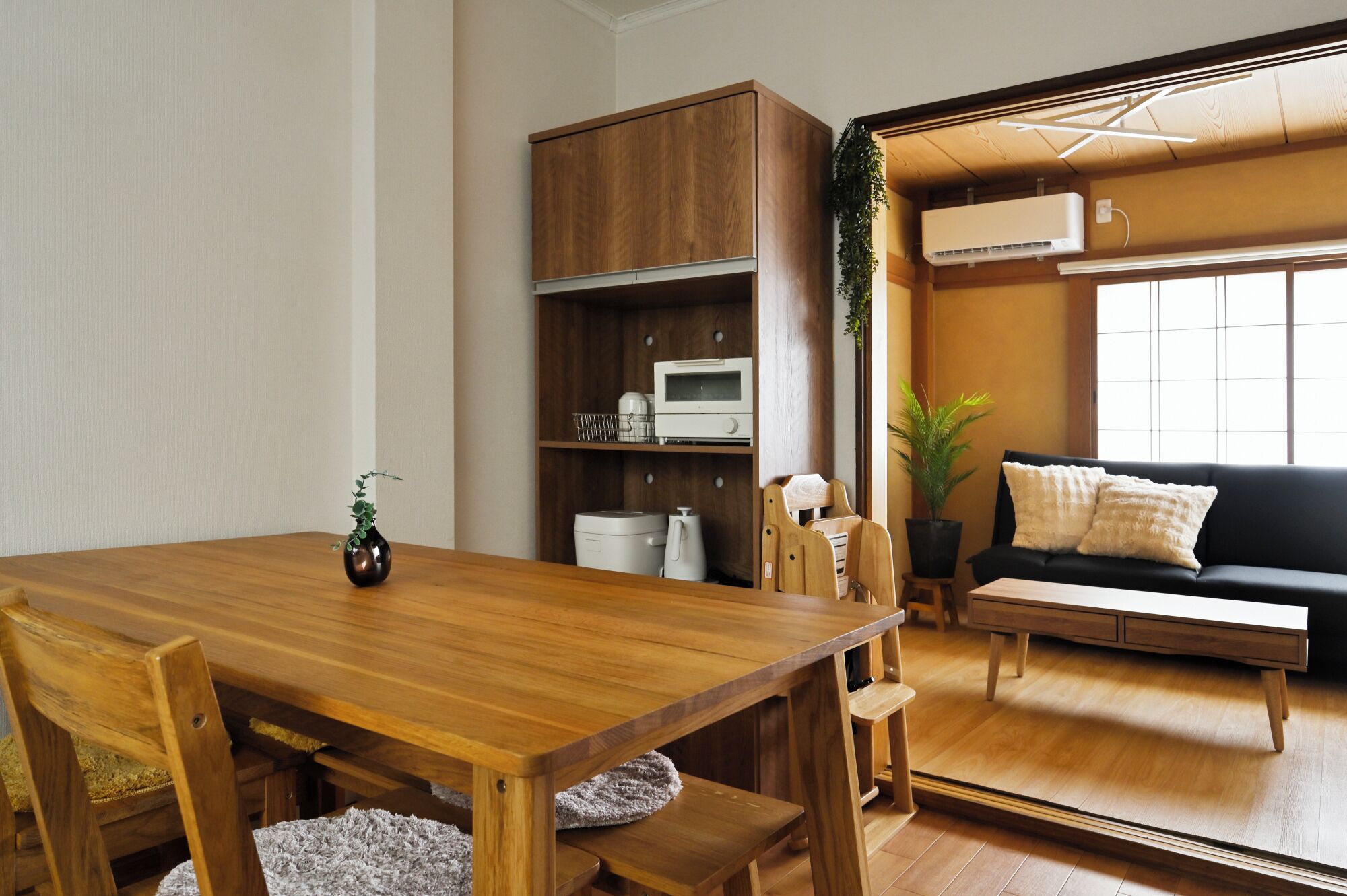 A wooden dining table with chairs, a built-in microwave, and a black sofa with cushions.