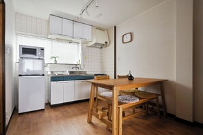 Eine kleine Küche mit weißen Schränken, einer Mikrowelle und einem Spülbecken. Ein Holztisch mit Stühlen steht daneben.