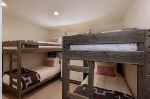 Dormitorio con literas, cabecera de madera, cómoda pequeña y pared lisa.