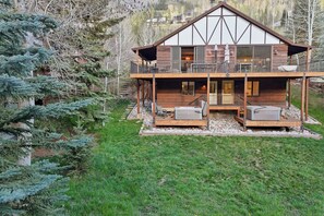 Eine zweistöckige Holzhütte mit Balkon, Sitzgelegenheit im Freien und einem Stein Fundament.
