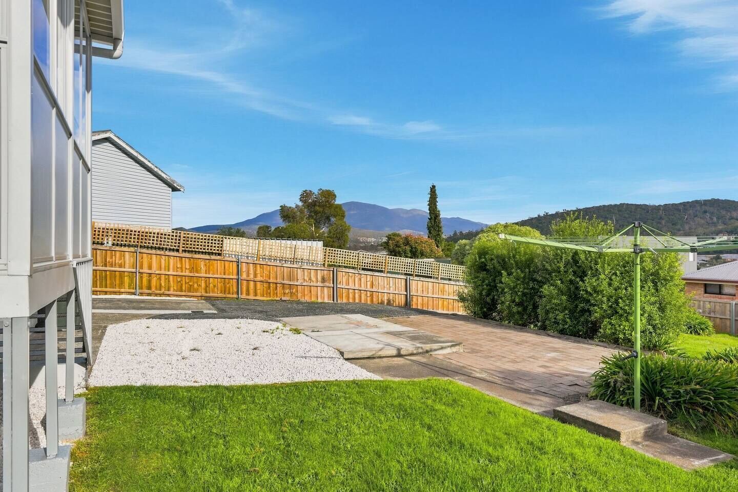 Patio trasero residencial con cercado de madera, césped y vista despejada de una cordillera al fondo.