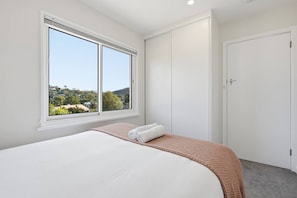 Ein Schlafzimmer mit einem großen Bett, einem Fenster mit Blick auf Grünflächen und einer geschlossenen Tür.