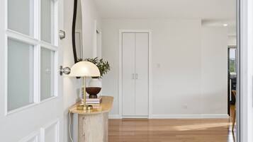 A hallway with a wooden floor, a white door, and a lamp on a wooden console.