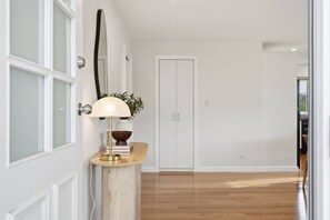 Ein Flur mit Holzboden, einer weißen Tür und einer Lampe auf einer Holzkonsole.