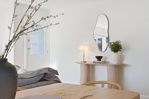 A room with a wooden dining table, a lamp, a mirror, a vase with a plant, and a door with frosted glass panels. - Modern 3BR Home Near Bellerive (Warrane)