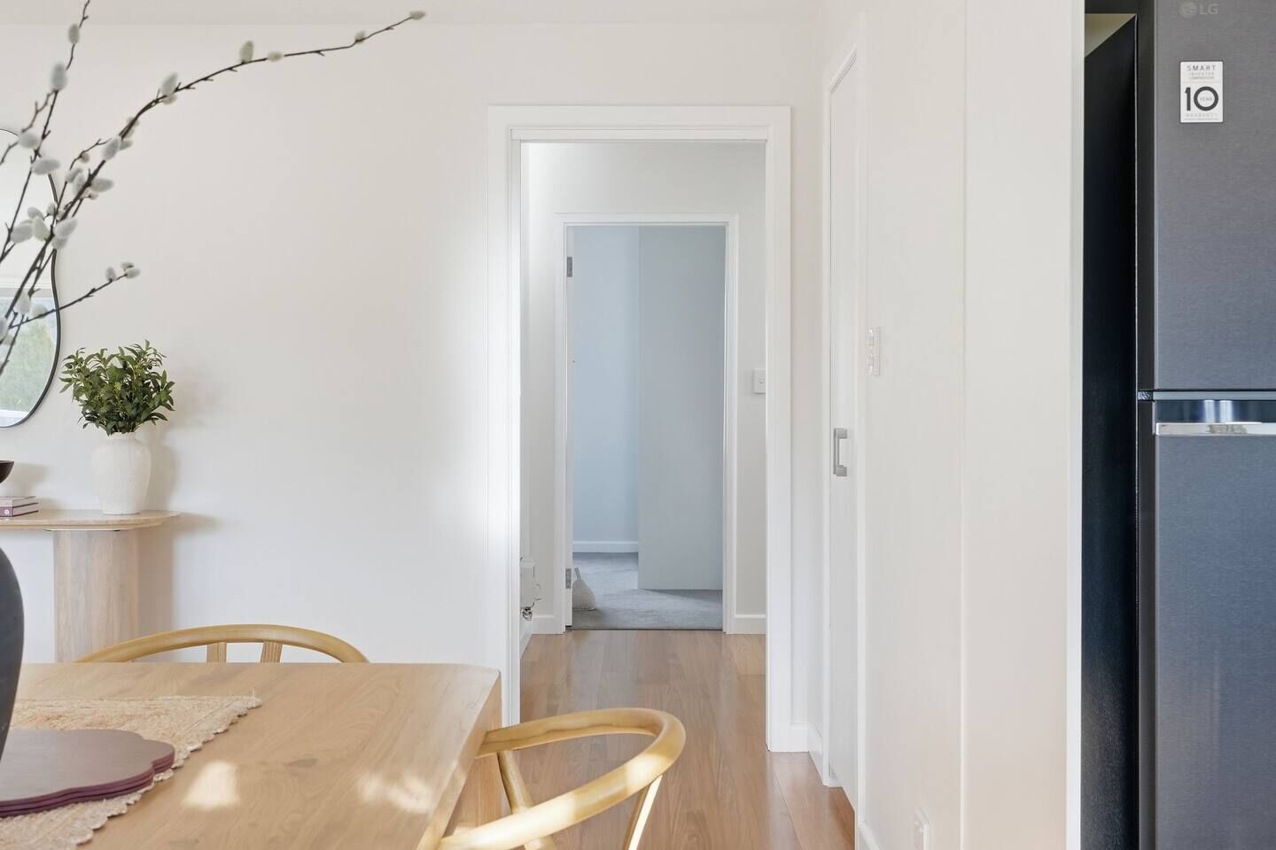 A modern kitchen with a black refrigerator, a dining table with chairs, and a hallway leading to another room.