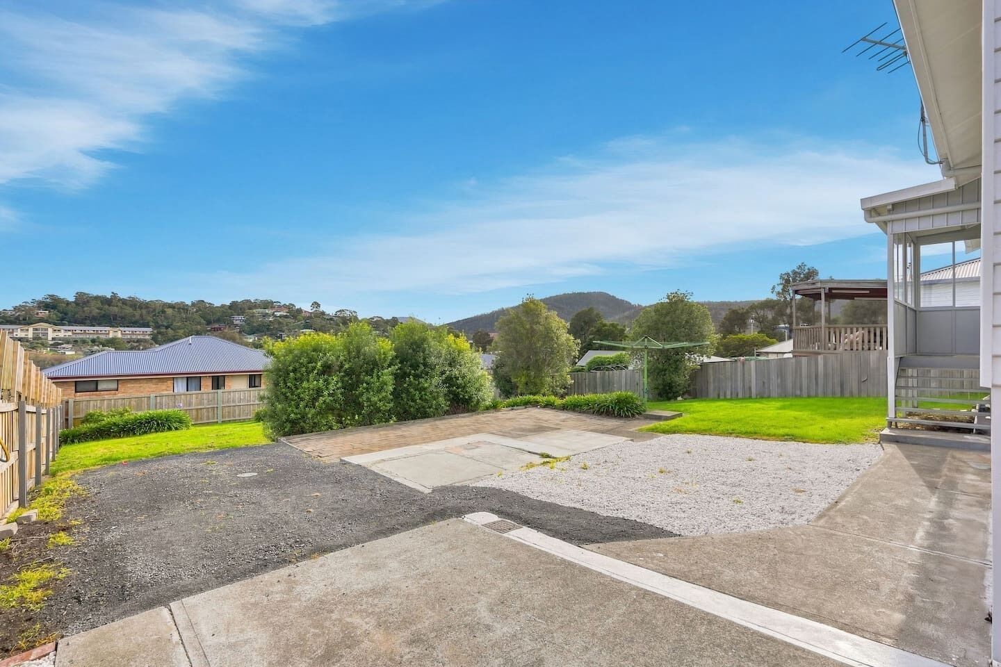 A residential backyard with a paved patio, a grassy lawn, and a wooden fence.
