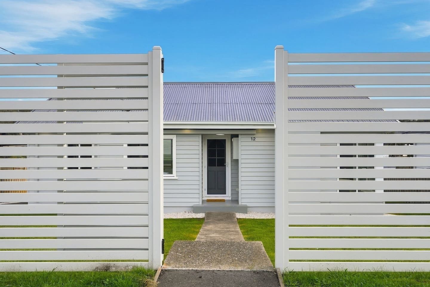 A modern house with a grey exterior, a metal roof, and a white fence with horizontal slats.