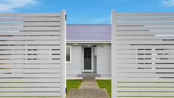 A modern house with a grey exterior, a metal roof, and a white fence with horizontal slats.