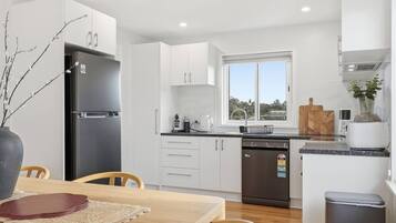 A modern kitchen with white cabinets, a black refrigerator, a dishwasher, and a window with a view.