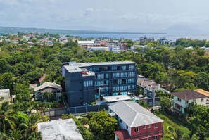 Un edificio de varios pisos con piscina, rodeado de vegetación exuberante y vista al mar.