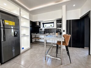 Eine moderne Küche mit Edelstahl-Kühlschrank, einem Einbauofen und einer Bar mit Sitzhocker.