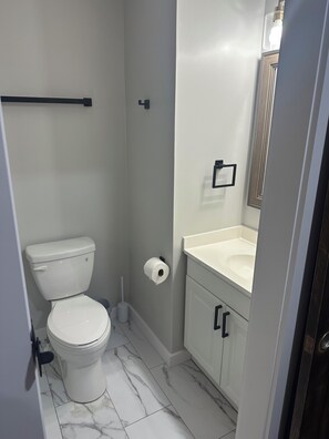 Une salle de bain comprenant des toilettes, un rouleau de papier toilette, un porte-serviettes et un miroir.