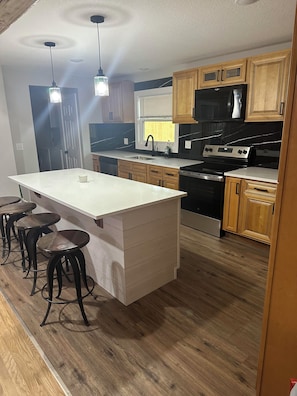 A kitchen with a central island, wooden cabinets, a black stove, and bar stools. - The Phoggy Cottage (Lawrence)