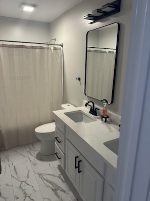 A bathroom with a toilet, a sink with a mirror, and a shower curtain. - The Phoggy Cottage (Lawrence)