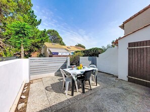 Ein Terrassenbereich mit Tisch und Stühlen, ein weißer Zaun und ein Gebäude mit einem Ziegeldach im Hintergrund.