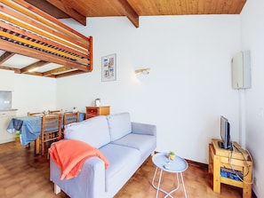 Uma sala de estar com sofá, mesa de jantar, cadeiras, rack para TV e uma pequena mesa com uma planta.
