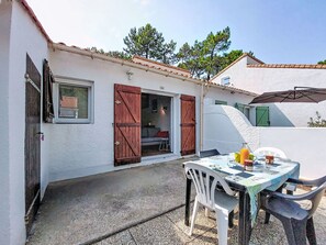 A white building with a tiled roof, a table with chairs, and a bottle of orange juice. - Les Maisons de l'Océan by Interhome (Les Mathes)