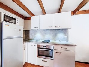 Uma cozinha compacta com armários brancos, forno embutido e micro-ondas.