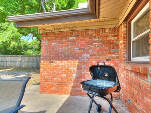 Ein Garten mit Ziegelmauer, Grill und überdachter Terrasse.
