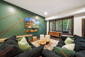 A modern living room with a large painting, a foosball table, and a sofa with cushions. - Legacy Springs at Eagles Nest - hot tub, creek (Banner Elk)