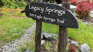 A wooden sign for Legacy Springs Trail, surrounded by greenery and a building in the background. - Legacy Springs at Eagles Nest - hot tub, creek (Banner Elk)