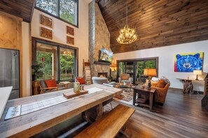 A spacious living area with a large wooden table, comfortable seating, a fireplace, and a stone wall. - Legacy Springs at Eagles Nest - hot tub, creek (Banner Elk)