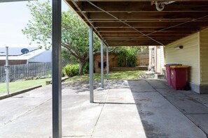 Un espace extérieur abrité, doté d’un sol en béton, de poutres métalliques et d’un plafond en bois.