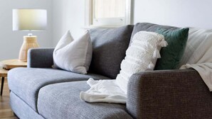 A grey sofa with a white throw blanket and a green pillow. - Lovely Family Home in South Launceston - Prime Location (South Launceston)