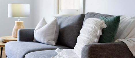 Un sofá gris con una manta blanca y un cojín verde.