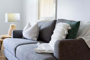Ein graues Sofa mit einer weißen Decke und einem grünen Kissen.