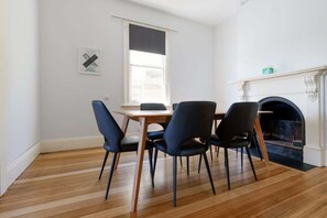 Un coin repas avec une table en bois et quatre chaises, une cheminée et une fenêtre avec des stores.