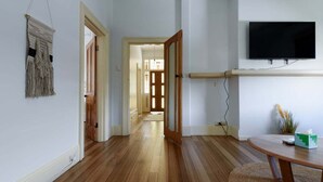 A hallway with wooden flooring, a flat-screen TV mounted on the wall, and a door leading to another room. - Lovely Family Home in South Launceston - Prime Location (South Launceston)