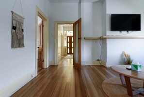 Ein Flur mit Holzboden, einem an der Wand montierten Flachbildfernseher und einer Tür zu einem weiteren Zimmer.