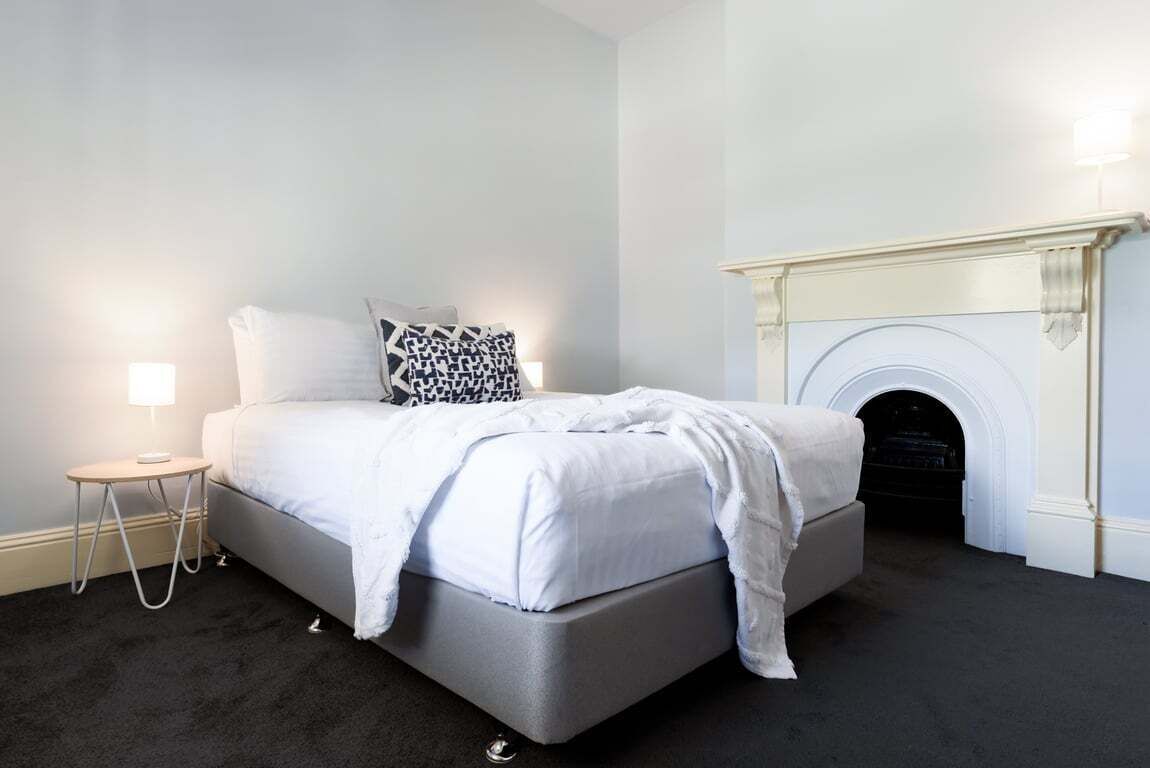 A bedroom with a bed, a bedside lamp, a patterned pillow, and a fireplace.
