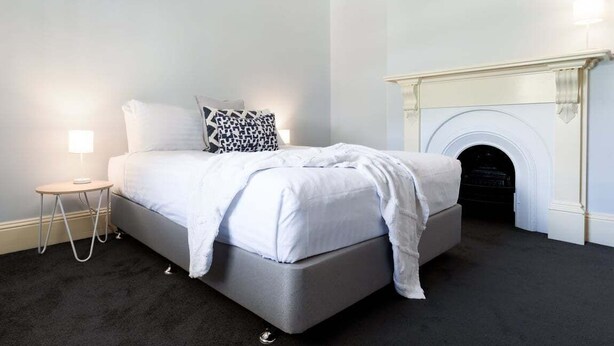 A bedroom with a bed, a bedside lamp, a patterned pillow, and a fireplace. - Lovely Family Home in South Launceston - Prime Location (South Launceston)