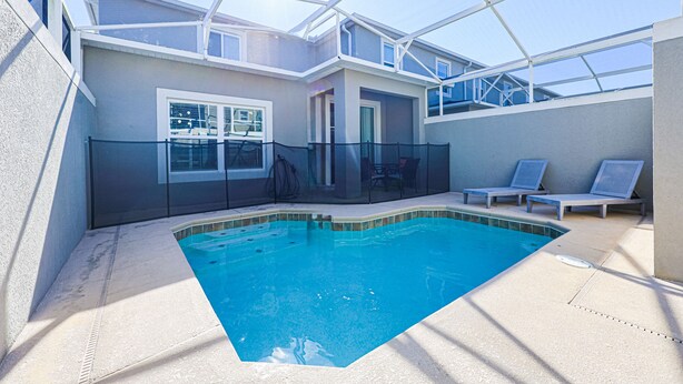 A swimming pool with a clear blue water, surrounded by a covered patio area with lounge chairs. - Sweet Home Near Disney —5BR Resort Villa + Private Pool (Kissimmee)