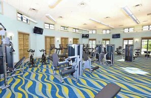 Ein Fitnessstudio mit unterschiedlichen Trainingsgeräten, großen Fenstern und einem gemusterten Teppich.