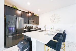 A modern kitchen with dark cabinets, stainless steel appliances, a central island with bar stools, and a wall clock. - 5BR Near Disney  with Private Pool & Resort Amenities (Kissimmee)