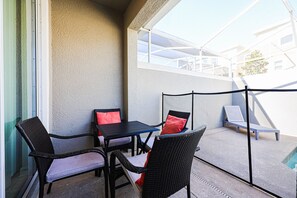 Un balcon avec des fauteuils en osier, une petite table et une chaise bleue avec un coussin rouge.