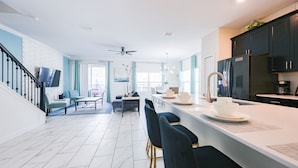 A modern kitchen with a central island, bar stools, and a dining area with a table and chairs. - Sweet Home Near Disney —5BR Resort Villa + Private Pool (Kissimmee)