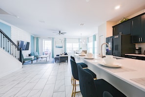 A modern kitchen with a central island, bar stools, and a dining area with a table and chairs. - Sweet Home Near Disney —5BR Resort Villa + Private Pool (Kissimmee)