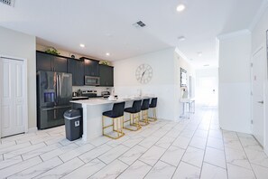 A modern kitchen with a central island, bar stools, and a wall clock. - 5BR Near Disney  with Private Pool & Resort Amenities (Kissimmee)