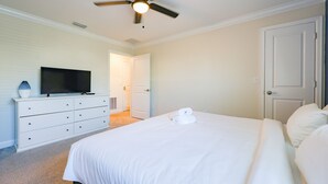 A bedroom with a bed, a dresser, a television, and a ceiling fan. - Sweet Home Near Disney —5BR Resort Villa + Private Pool (Kissimmee)
